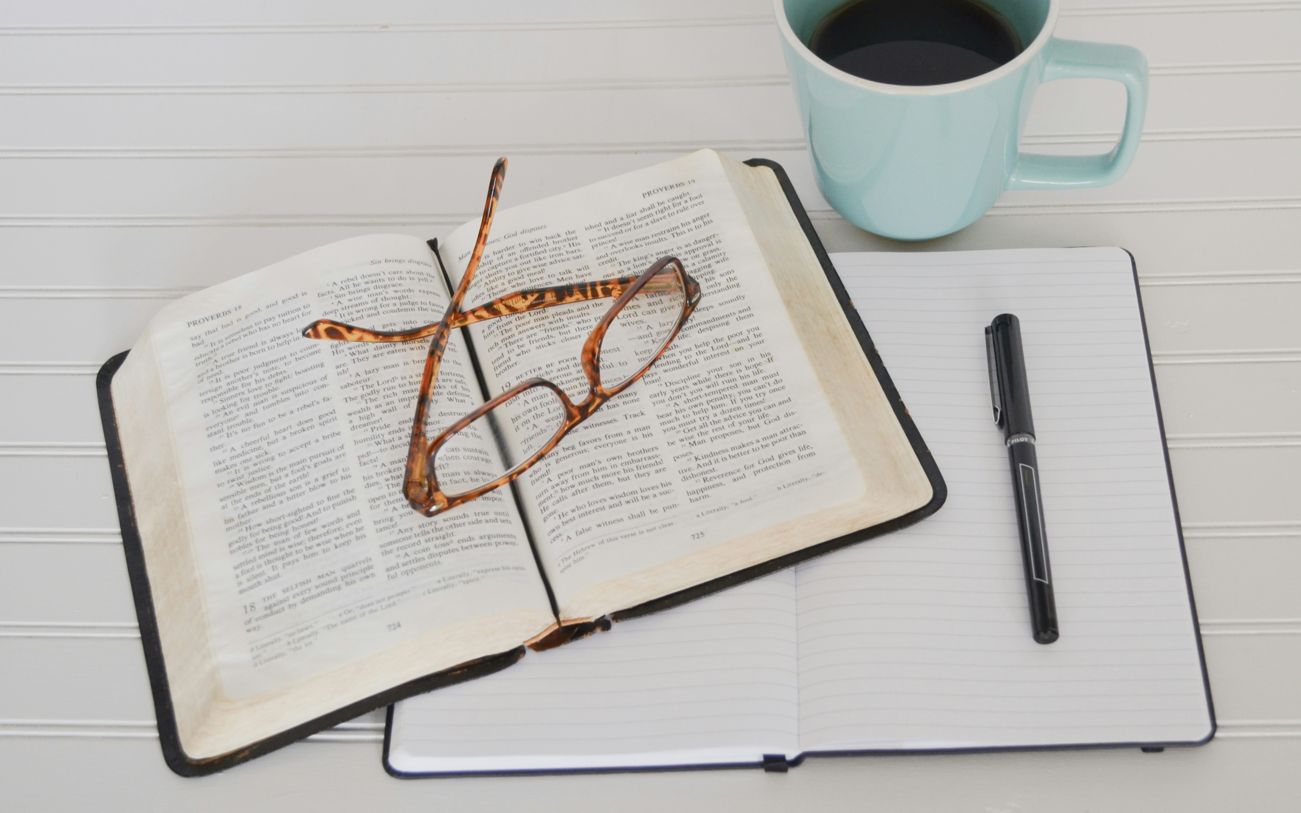 Bible verses for thankfulness - A top view of a Bible, Notebook, Pen, Glasses and Coffee Mug
