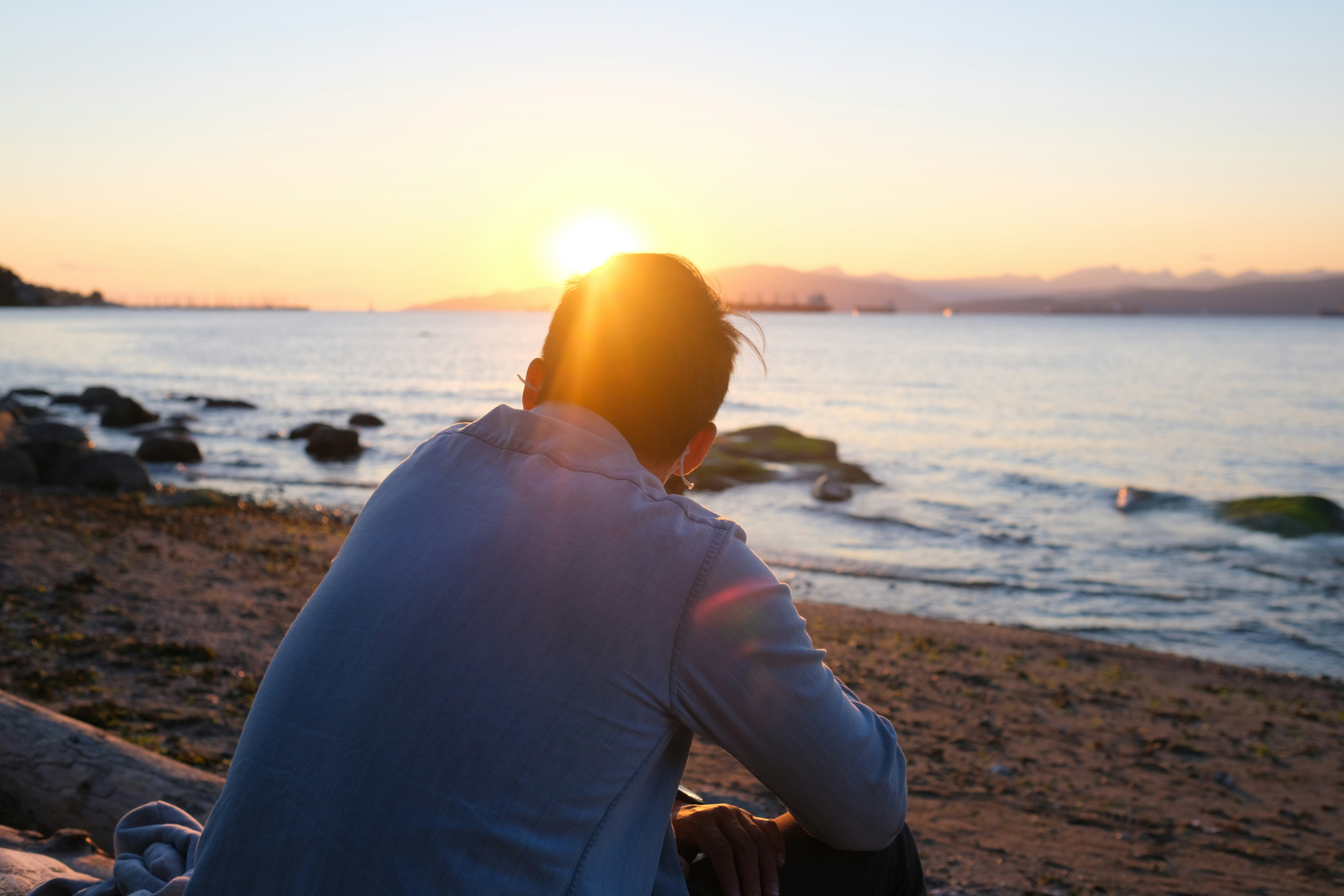 practicing gratitude when it feels hard - contemplative man looking at the sea at sunset, viewed from behind
