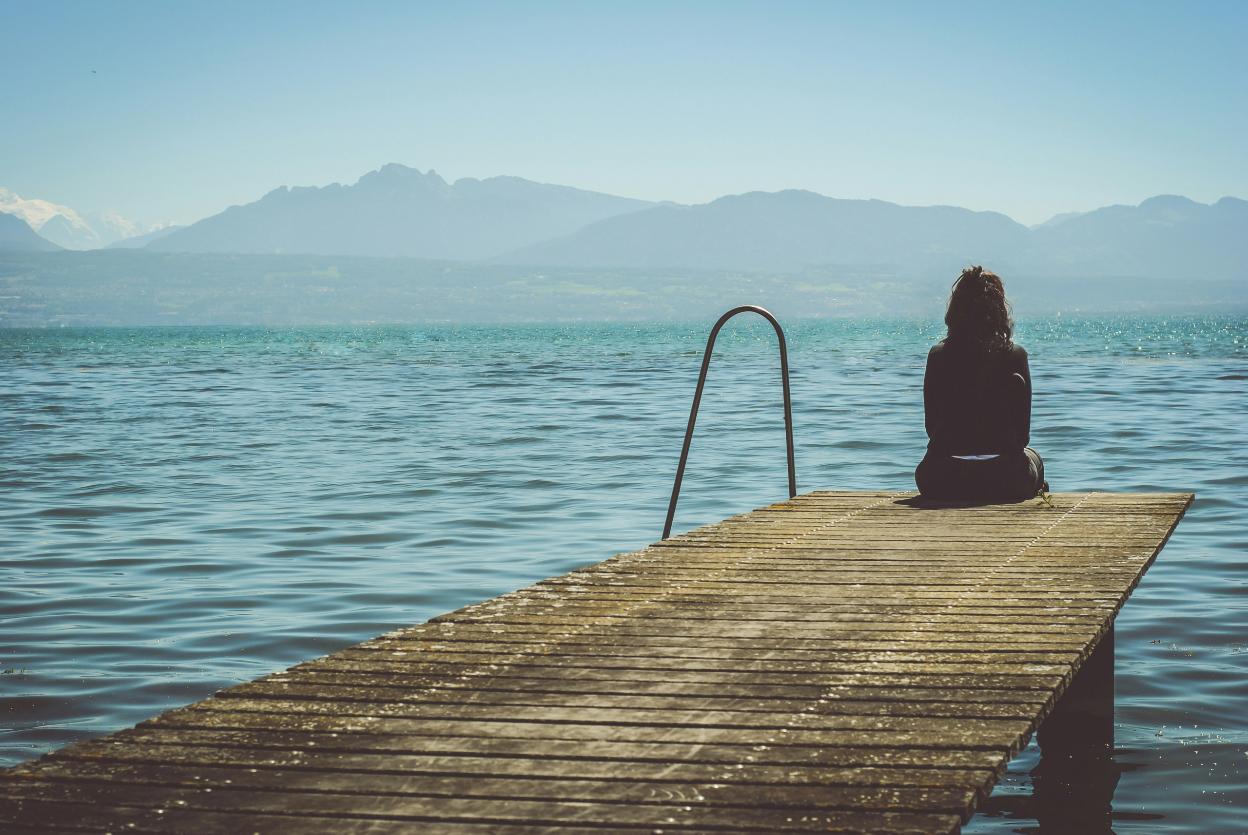 how to stop comparing yourself to others - woman sitting at the edge of a pier, view from behind.