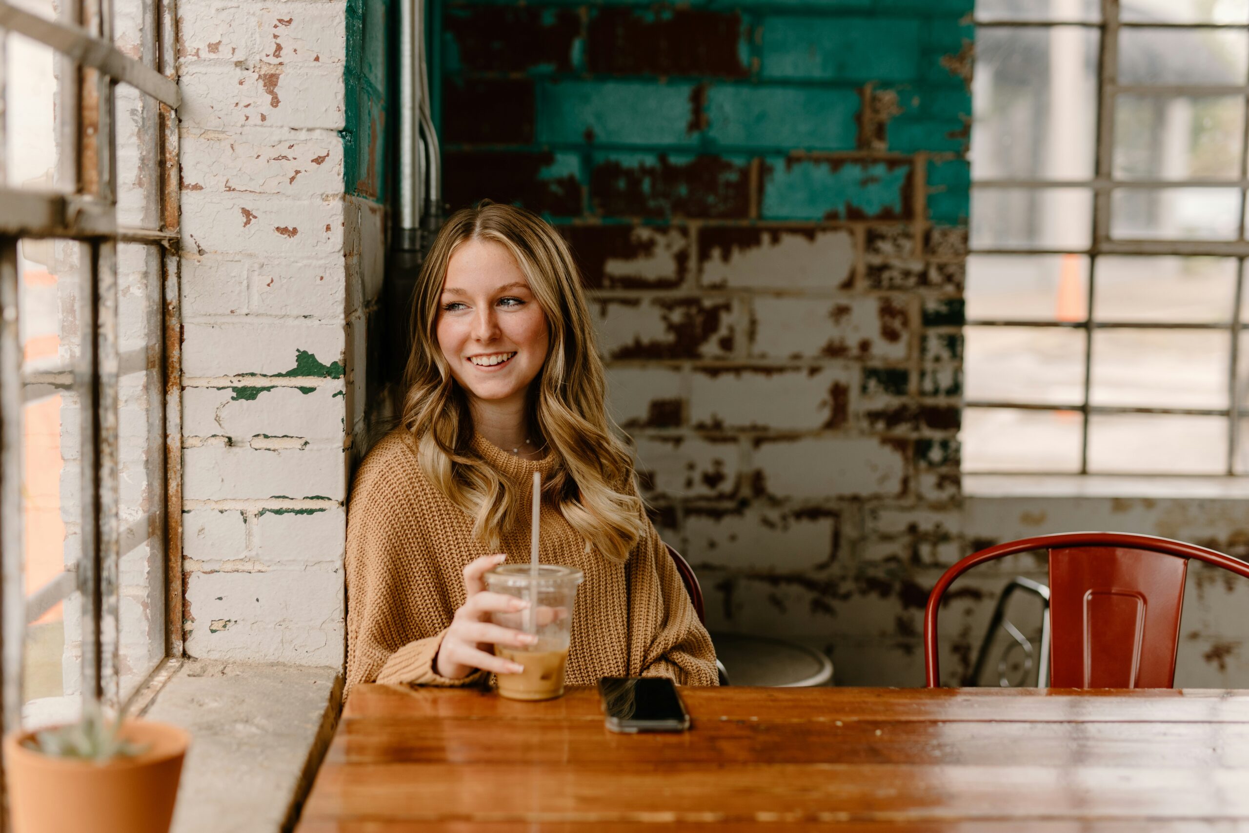 how to feel better when emotionally drained - woman drinking a cold drink at a café while looking out of the window and smiling
