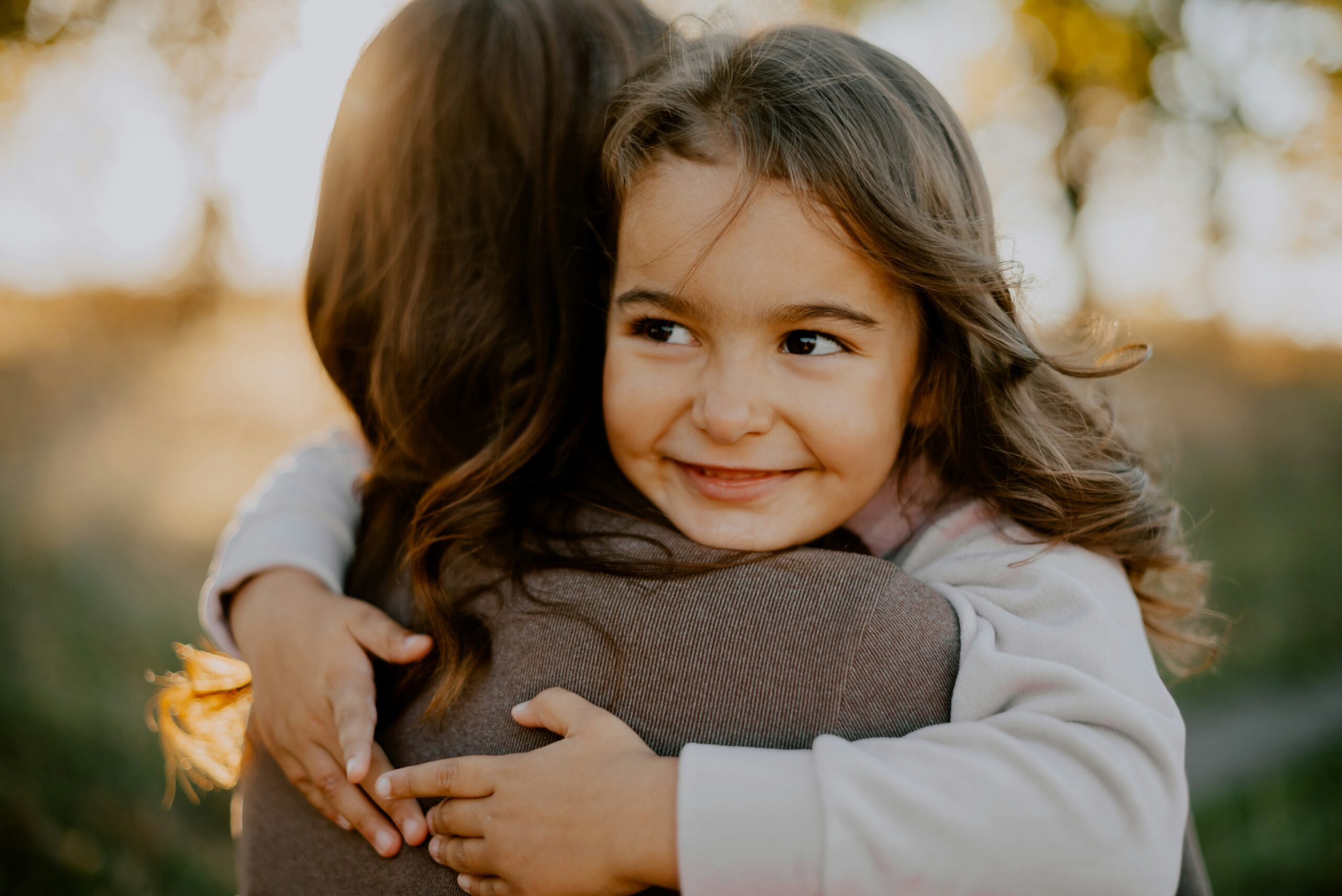 how to be more present with your children - mother holding her smiling daughter in a park just before sunset
