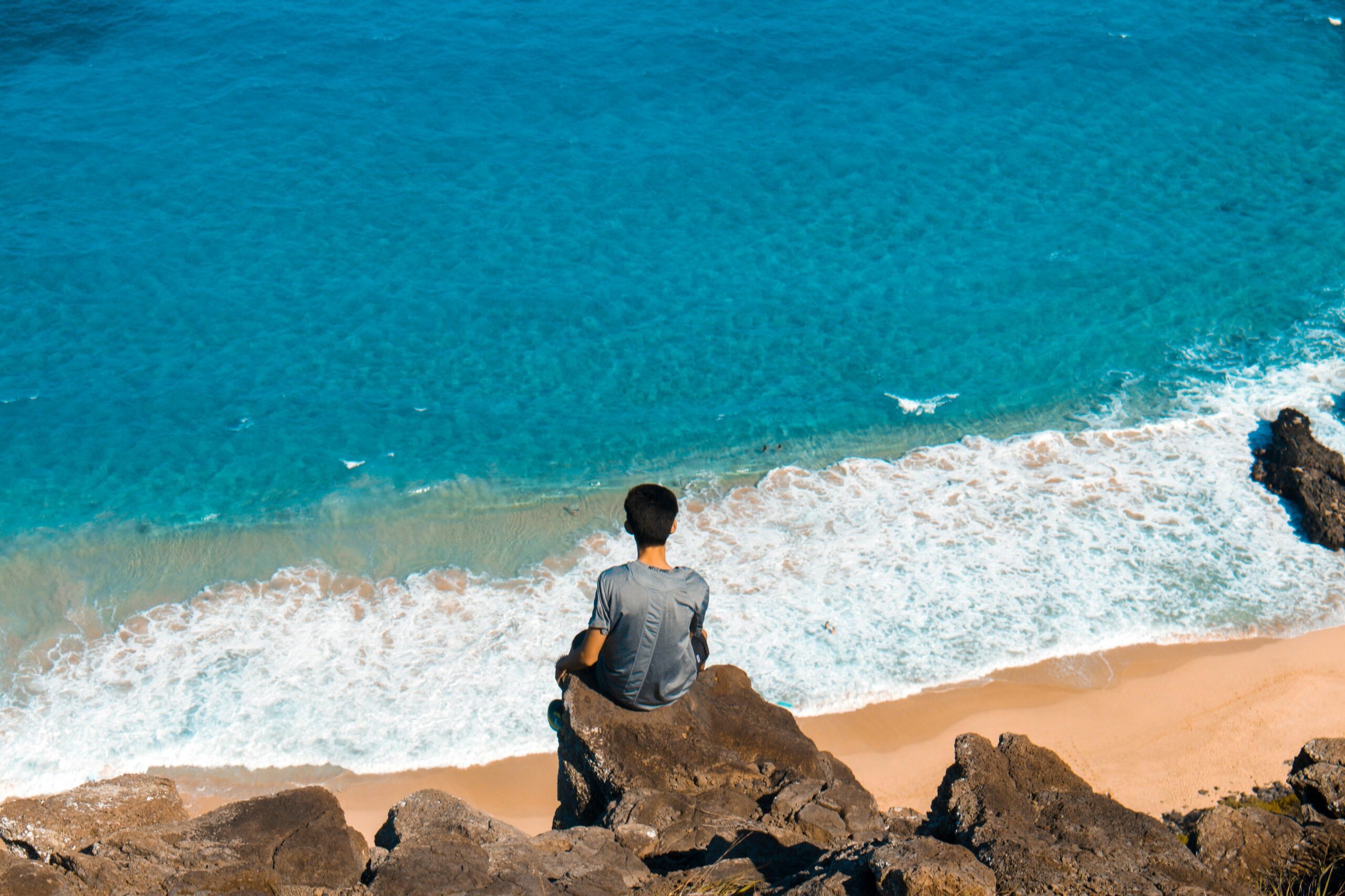 how to stop overthinking things you can't control - man sitting on the edge of a small cliff looking out toward the sea