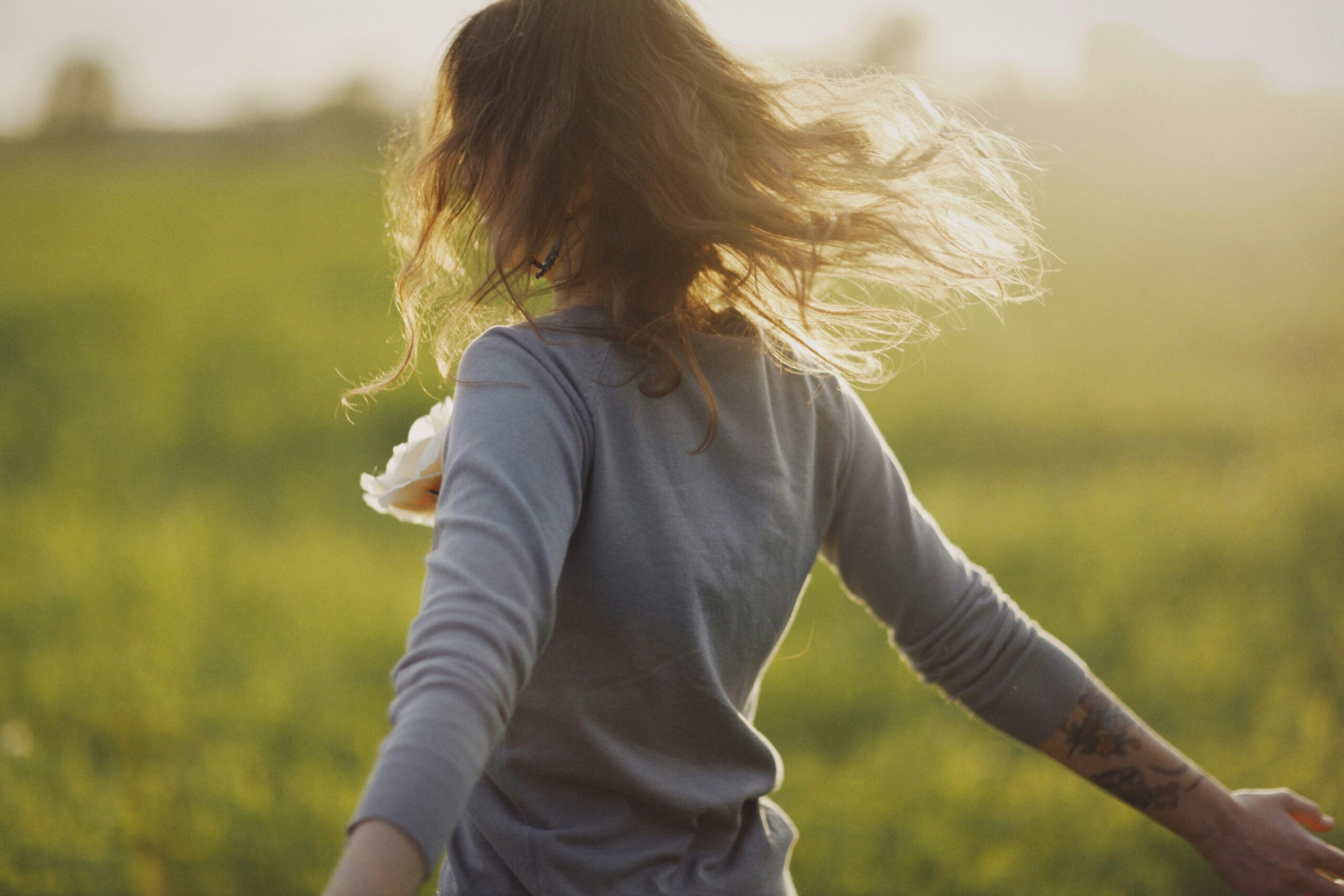 Enjoying life more - woman spinning in green field with golden light