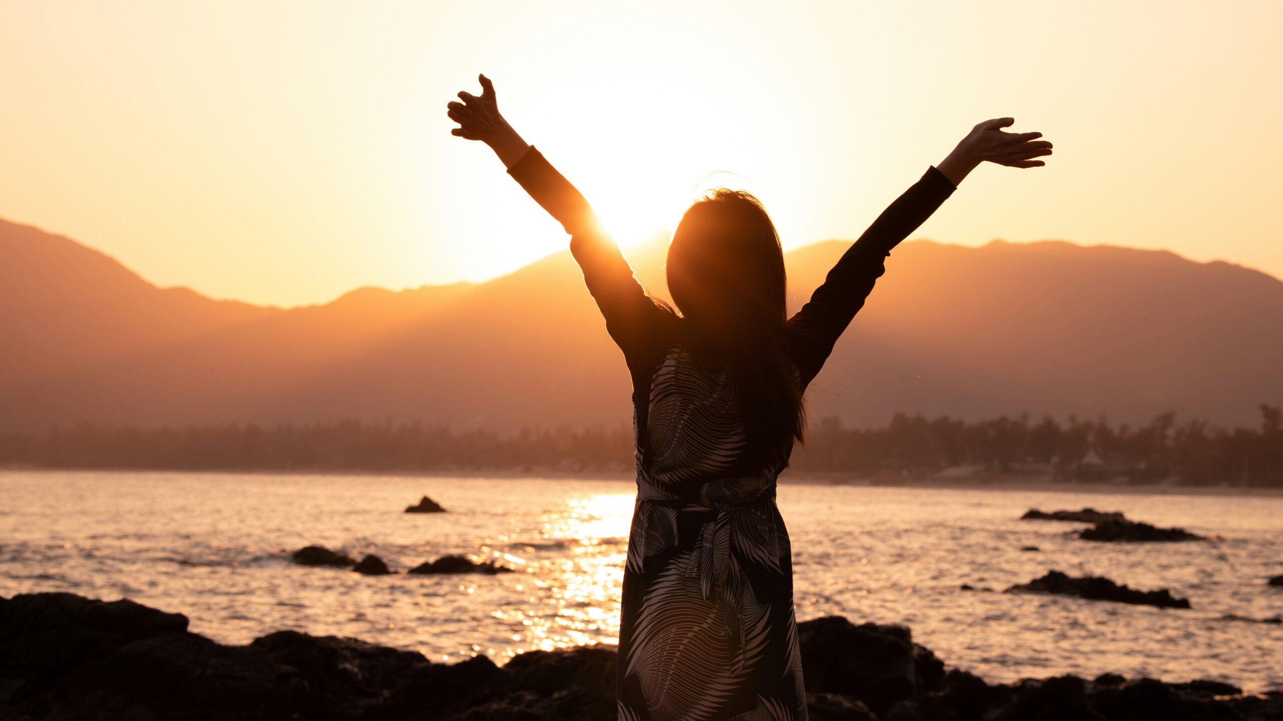 how to make life more meaningful - woman with hands up at the sea with beautiful sunset.