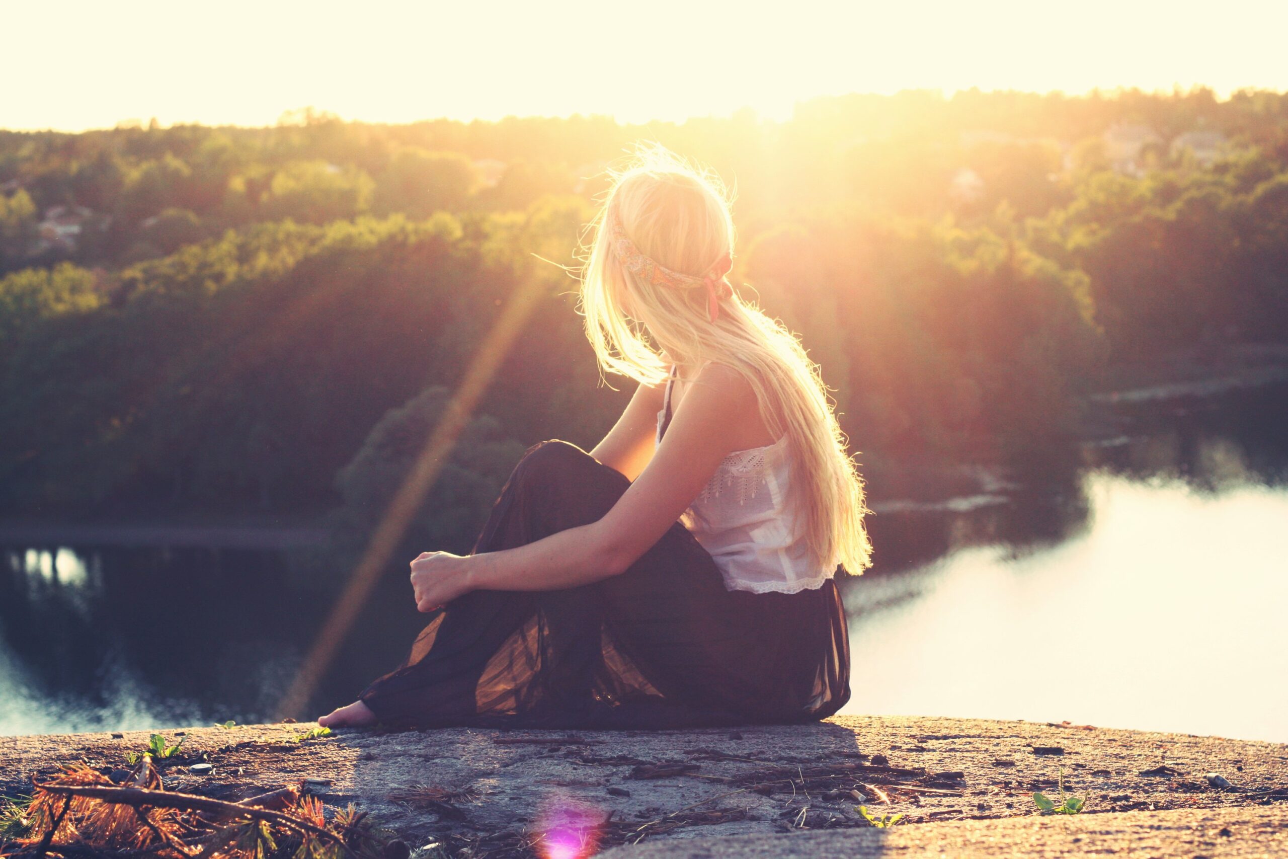 how to stop feeling stuck in life - Woman enjoying view of lake from an elevated rock at sunset