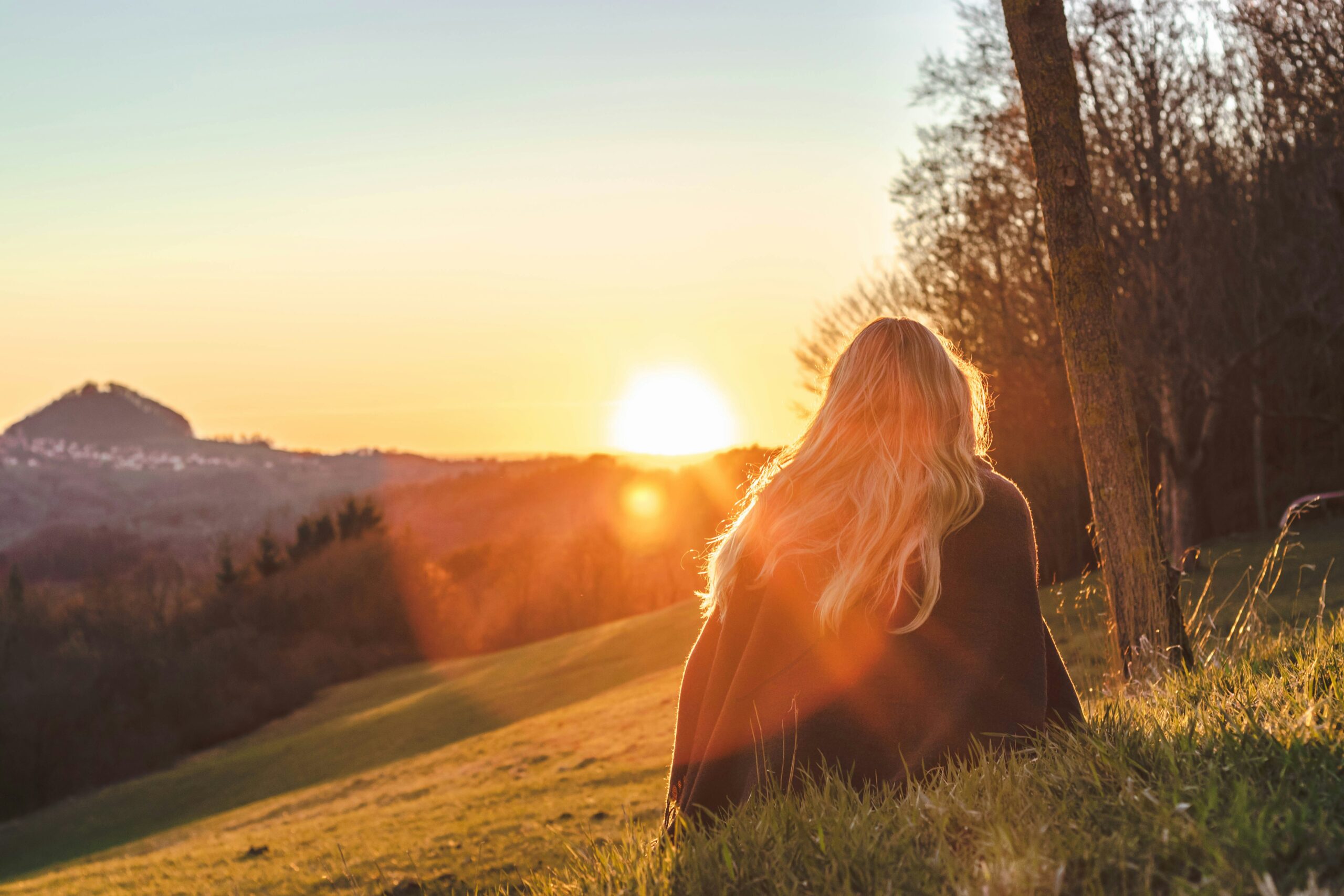 how to enjoy life more - Woman sitting on an elevated field admiring the sunset